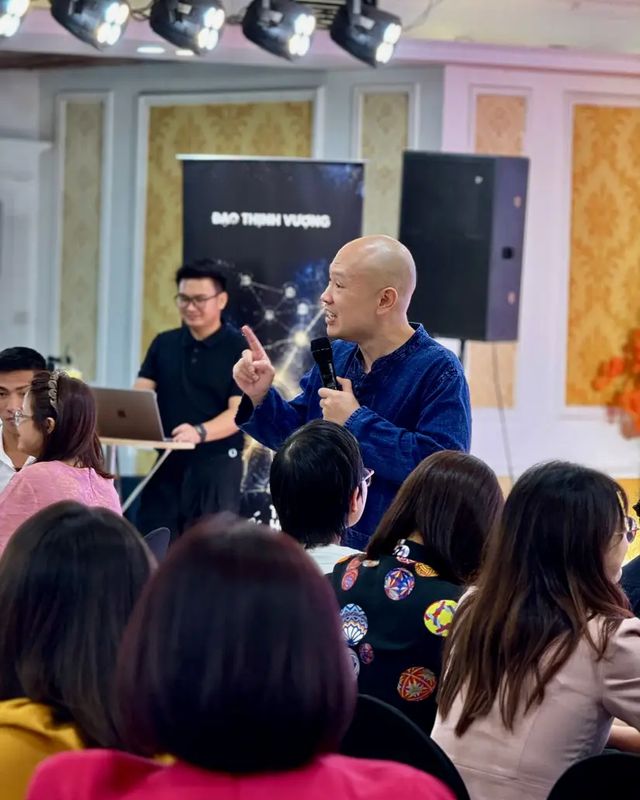 Anh Võ Hoài Nam cầm micro, giơ tay giảng giữa những người đang ngồi nghe trong một hội trường.